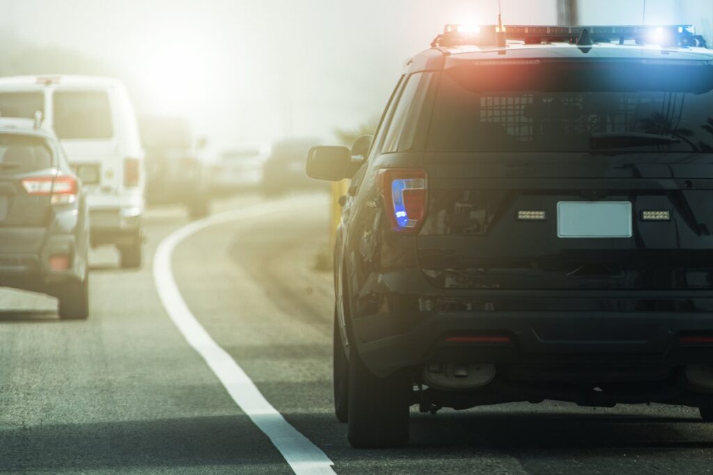 Highway patrol vehicle with emergency lights stopped on the shoulder of a road